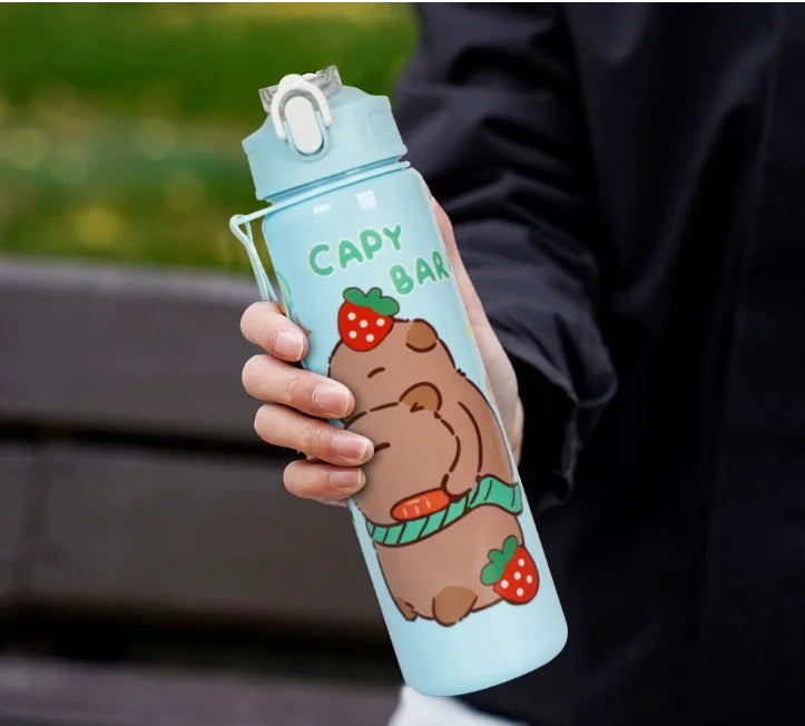 A hand holds a light blue water bottle featuring a cute brown capybara design with a strawberry and a green straw.