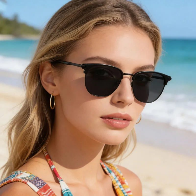 A woman wearing black vintage square metal frame sunglasses outdoors near the ocean
