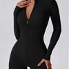 Model trägt einen schwarzen, langärmeligen, eng anliegenden Zip-Overall.