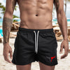 A muscular man wearing black quick-drying swim shorts with a red bull emblem.