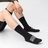 A close-up of black professional cycling and MTB socks being worn on a person's leg.