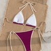 A purple and white two-piece bikini set laid out on a beige woven mat.