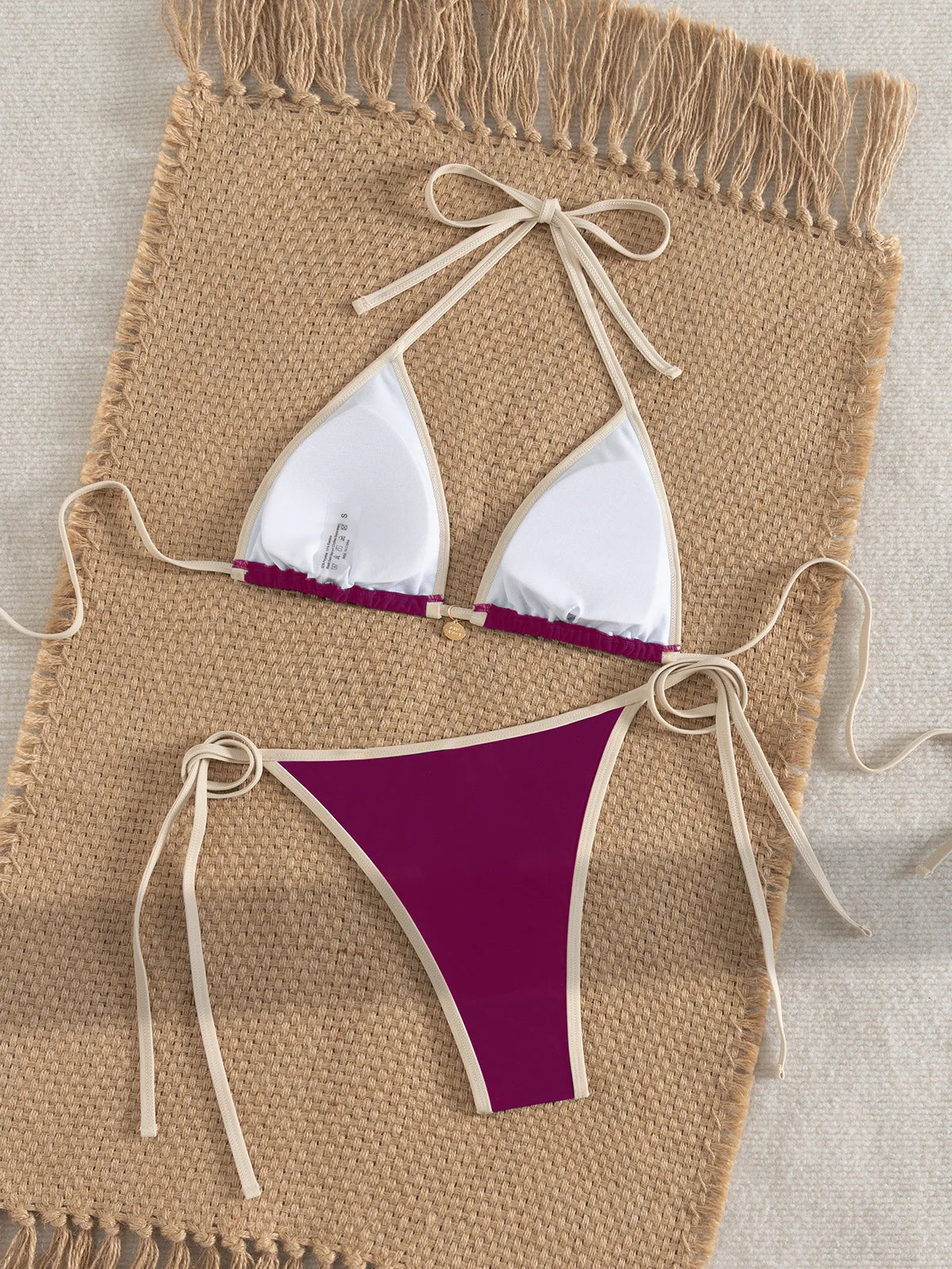 A purple and white two-piece bikini set laid out on a beige woven mat.