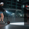 A woman rides a black electric scooter at night, with illuminated front and rear lights.