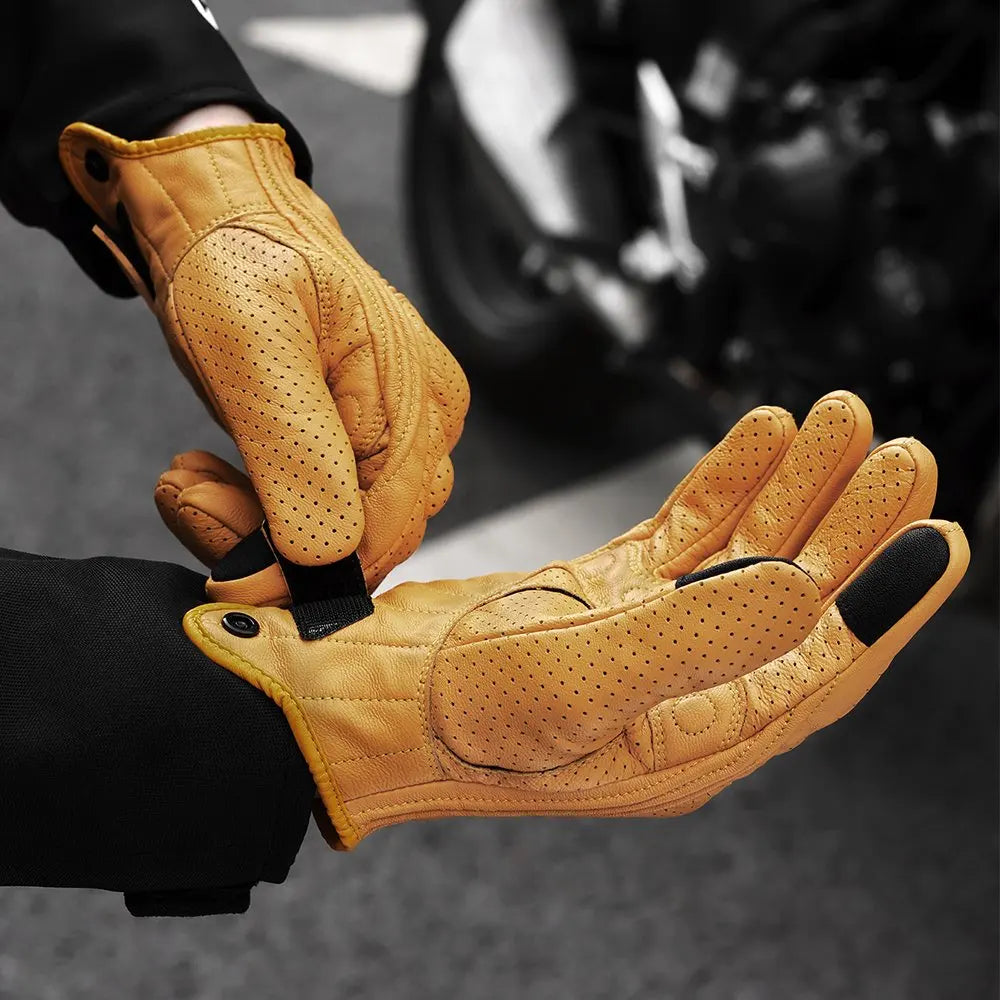 A close-up of tan vintage leather motorcycle riding gloves being held by a person.