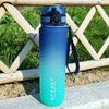 A tall, light blue sports water bottle with a black cap and strap is placed on a stone surface outdoors.