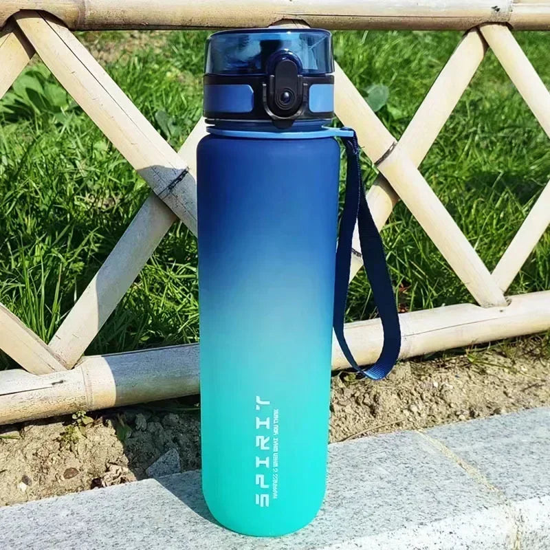 A tall, light blue sports water bottle with a black cap and strap is placed on a stone surface outdoors.