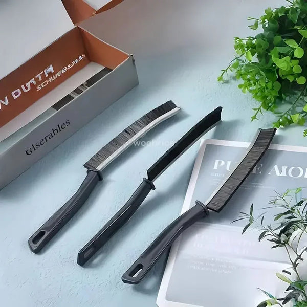A black hard bristle crevice cleaning brush is shown next to a box and some greenery.