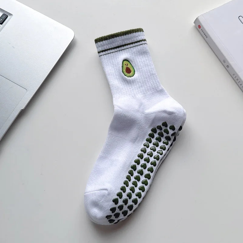 Chaussettes de yoga blanches avec broderie verte et motif antidérapant, posées sur une surface blanche.