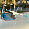 A pair of blue and clear sports sunglasses resting on a white surface outdoors.