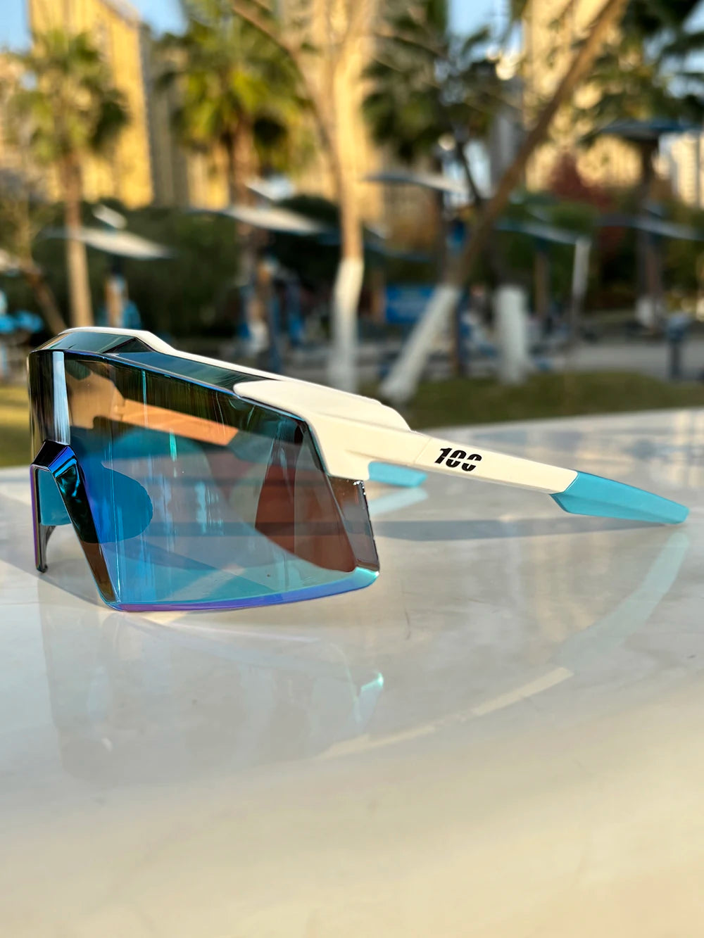 A pair of blue and clear sports sunglasses resting on a white surface outdoors.