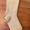 A beige therapeutic compression sock for the foot and ankle, shown flat on a wooden surface.