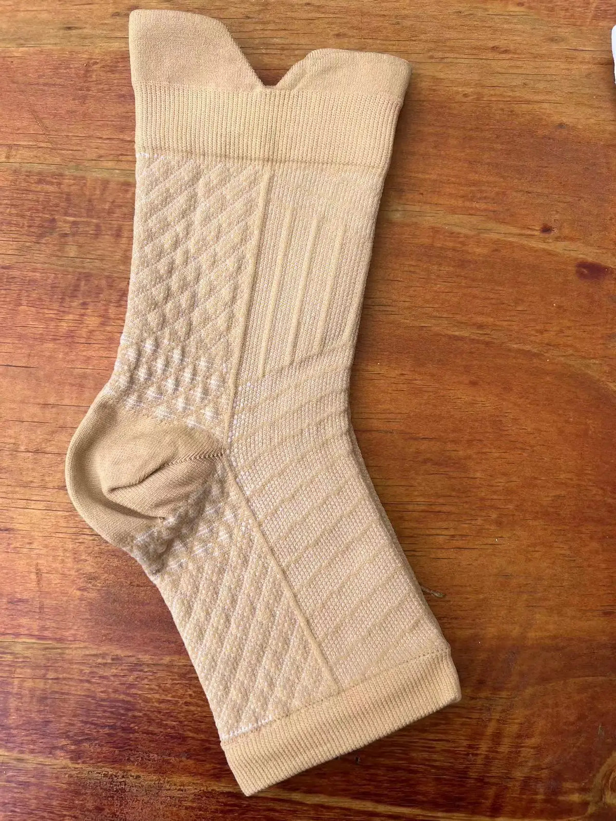 A beige therapeutic compression sock for the foot and ankle, shown flat on a wooden surface.