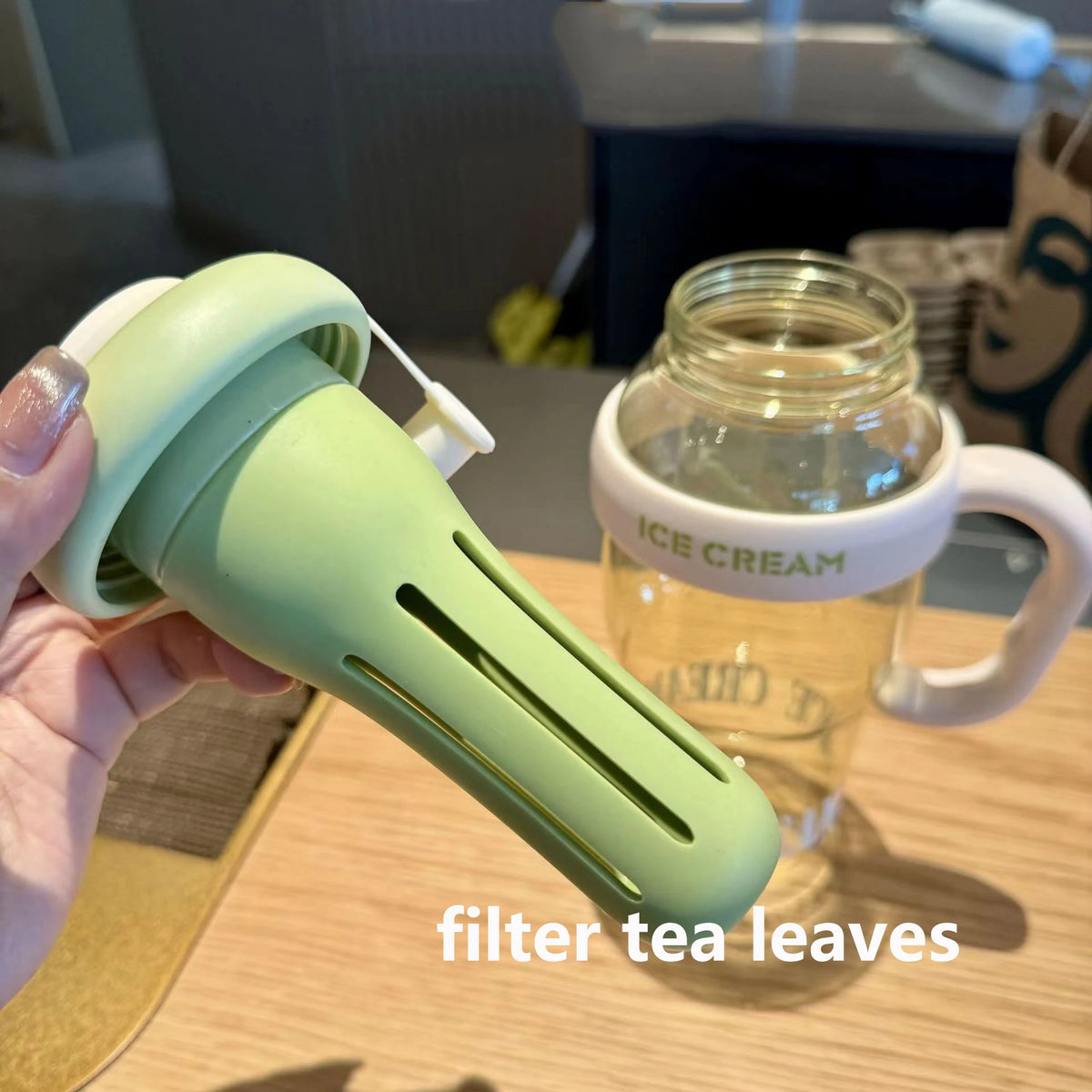A hand holds a light green reusable leak-proof water bottle with a straw and handle next to a jar of ice cream.