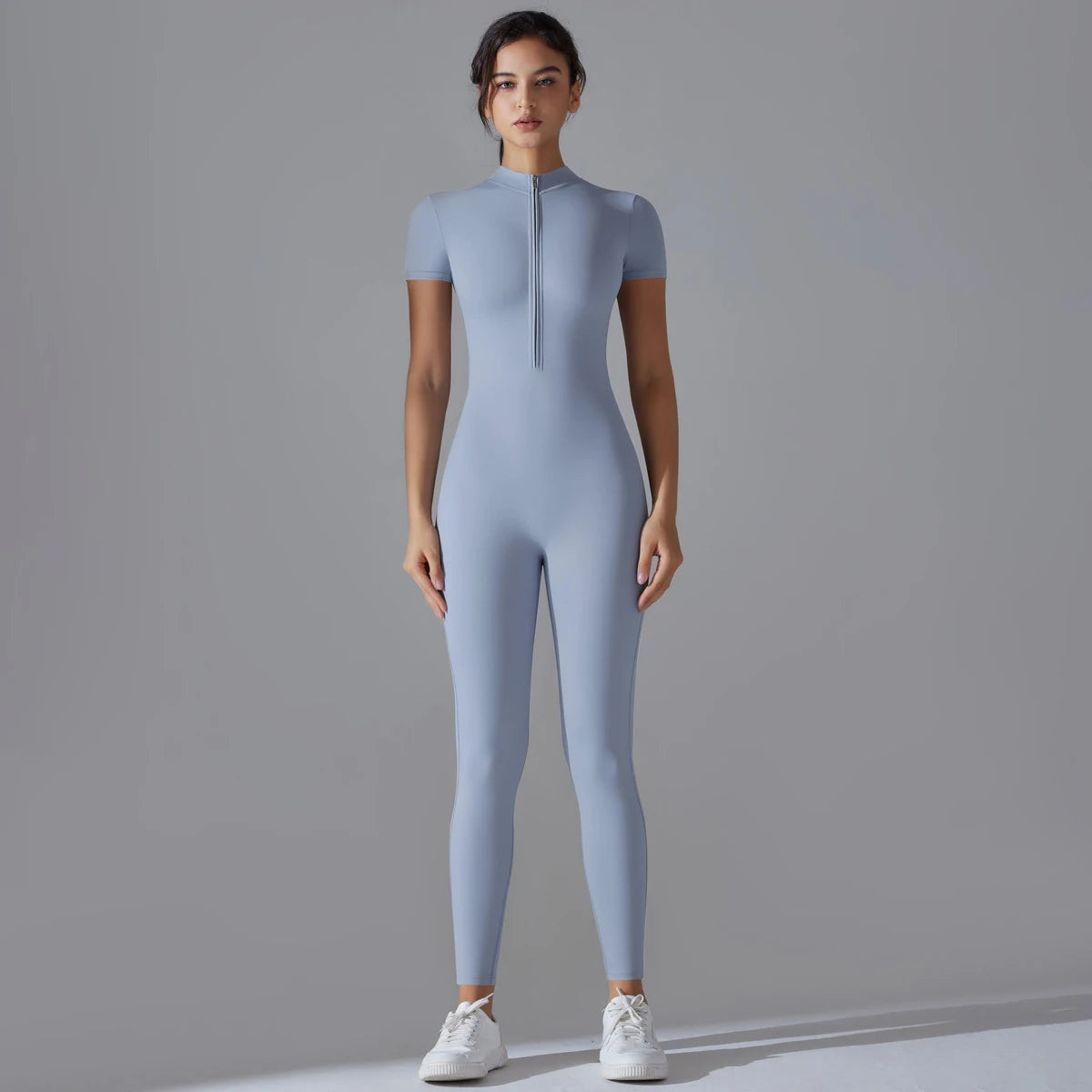 A model wearing a light blue Naked Zipper Yoga Jumpsuit standing against a gray background.