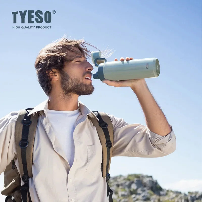 A man holds a light green insulated stainless steel water bottle outdoors against a blue sky.