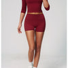 A model wearing a maroon women's yoga and fitness leggings set, featuring long sleeves and a cropped style.