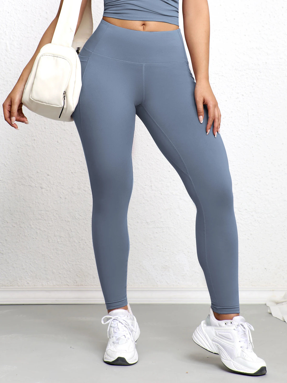 A woman wearing high-waisted gray sports leggings and a cropped top, standing indoors.