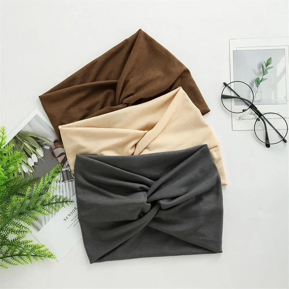 Three cross-knotted fabric headbands in brown, beige, and gray are displayed on a white surface.