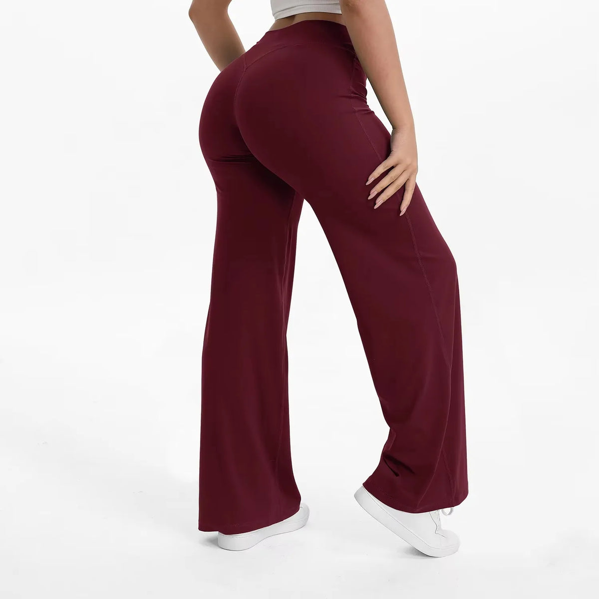 A model is wearing maroon high-waist yoga pants and a light gray top, standing in a studio setting.