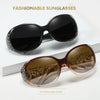 A pair of brown tinted sunglasses with diamond-inlaid detailing is displayed on a white surface.