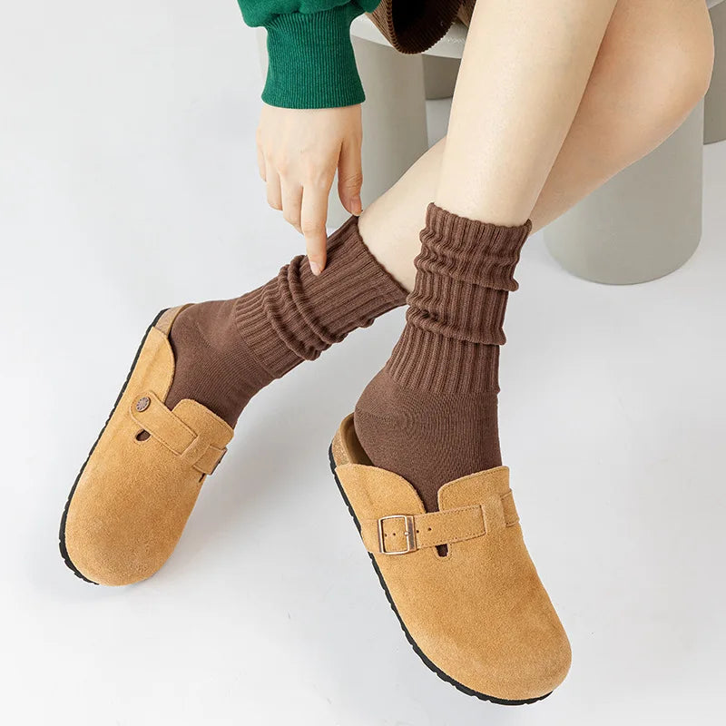 A person is wearing brown thick cotton tube socks and tan suede slip-on shoes.