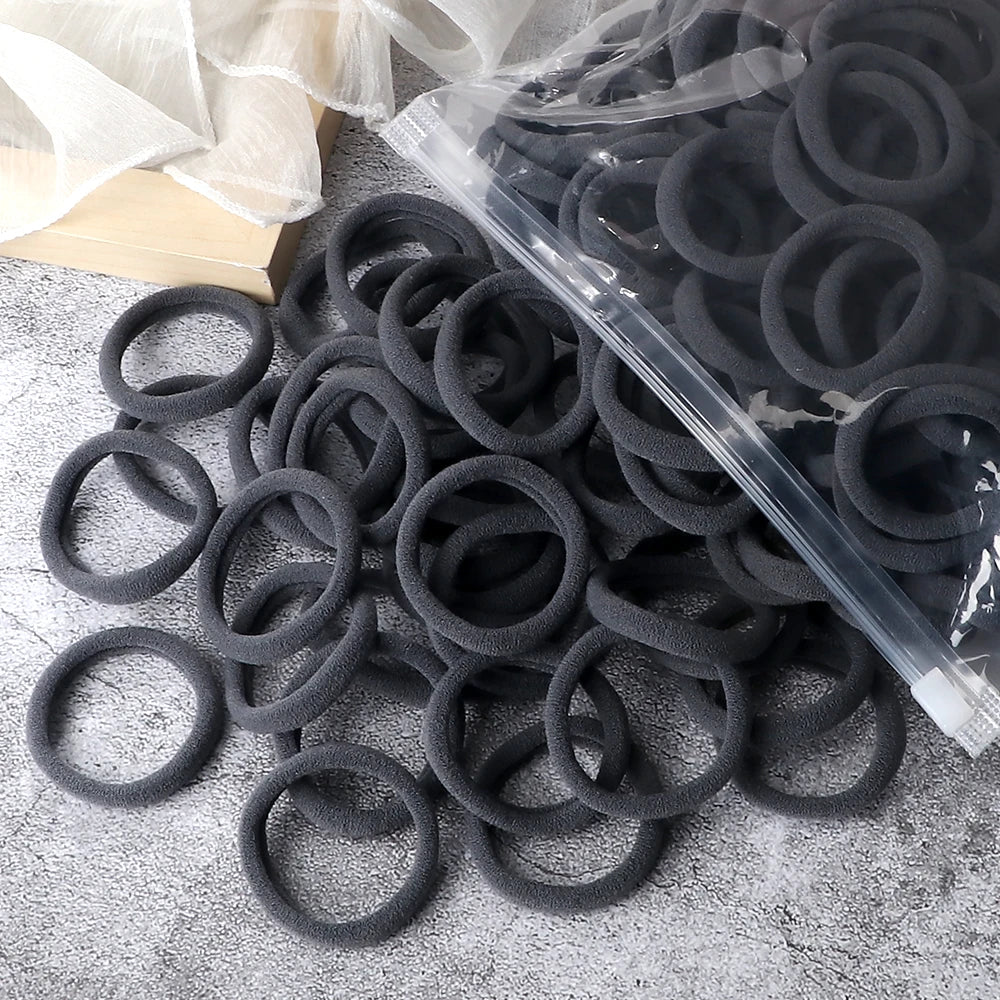 A pile of black elastic hair bands in a clear plastic bag on a gray surface.