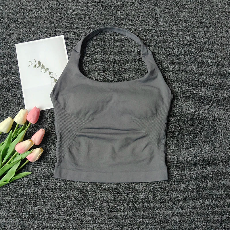 A gray seamless yoga and pilates sports bra is displayed on a dark gray textured surface next to pink and white tulips.