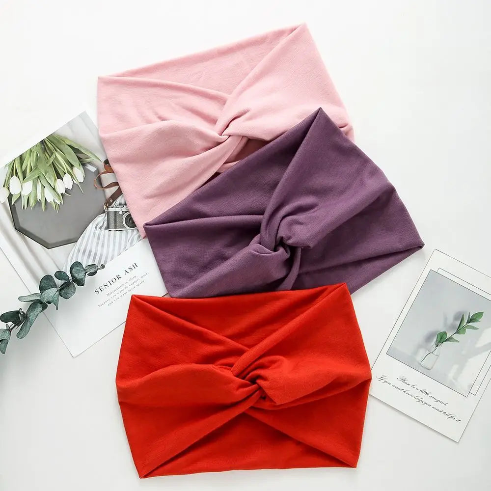 Three cross-knotted fabric headbands in pink, purple, and red laid on a white surface.