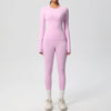 A woman wearing a long-sleeved pink performance yoga and gym set with matching leggings and white sneakers.