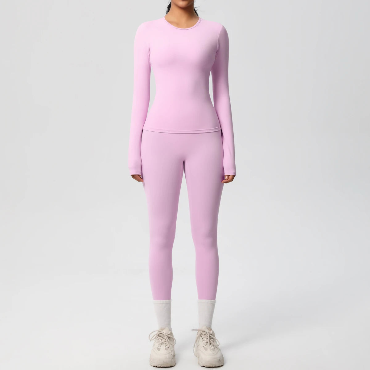 A woman wearing a long-sleeved pink performance yoga and gym set with matching leggings and white sneakers.