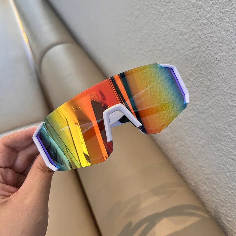 A hand holds a pair of orange and yellow tinted cycling sunglasses against a light background.