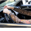 A close-up of a person driving a car, wearing long sleeves with colorful tattoo-style designs.