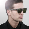 A male model wearing dark gray square polarized sunglasses in a studio setting.