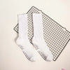 Pair of white mid-calf yoga and pilates socks with silver polka dots resting on a black grid mat.