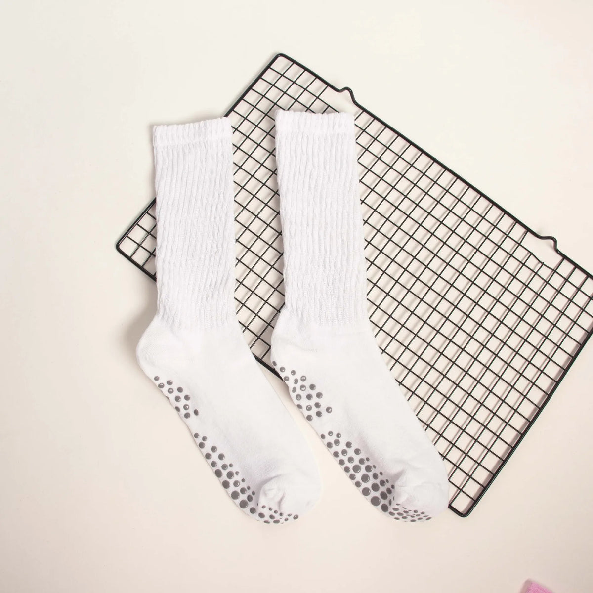 Pair of white mid-calf yoga and pilates socks with silver polka dots resting on a black grid mat.