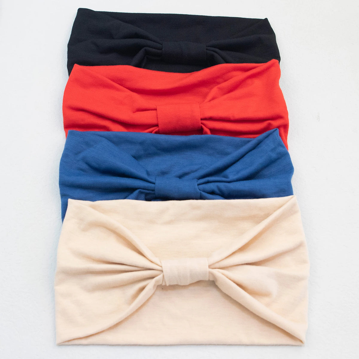 Ein Stapel von vier weichen elastischen breiten Stirnbändern in Schwarz, Rot, Blau und Beige.