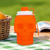 An orange skull-shaped leakproof sports water bottle with a white cap and orange straw, resting on a green checkered cloth.