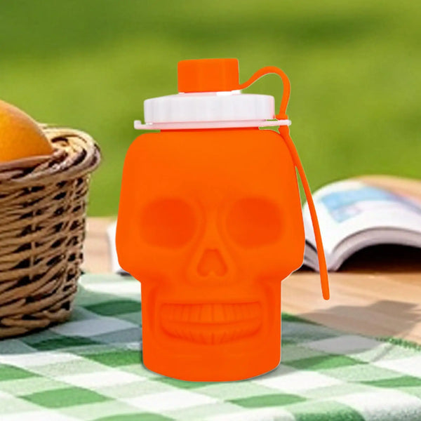 Botella deportiva impermeable con forma de cráneo naranja, tapa blanca y sorbete naranja, sobre un paño verde a cuadros.