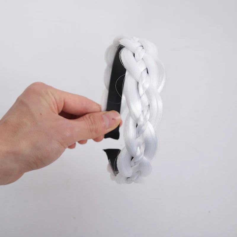 A hand is holding a twisted braided wig headband made of white hair and black elastic.