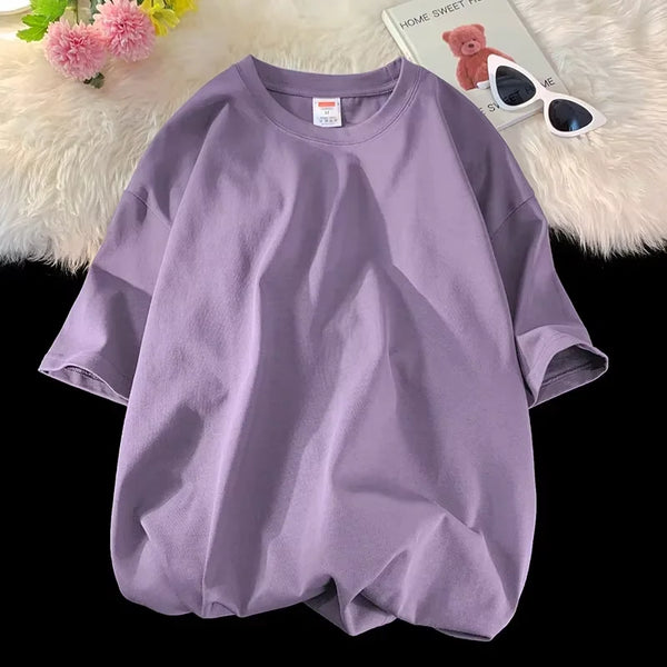 T-shirt ample violet clair de coton pour femme, posé sur une surface blanche et duveteuse avec des lunettes de soleil et des 