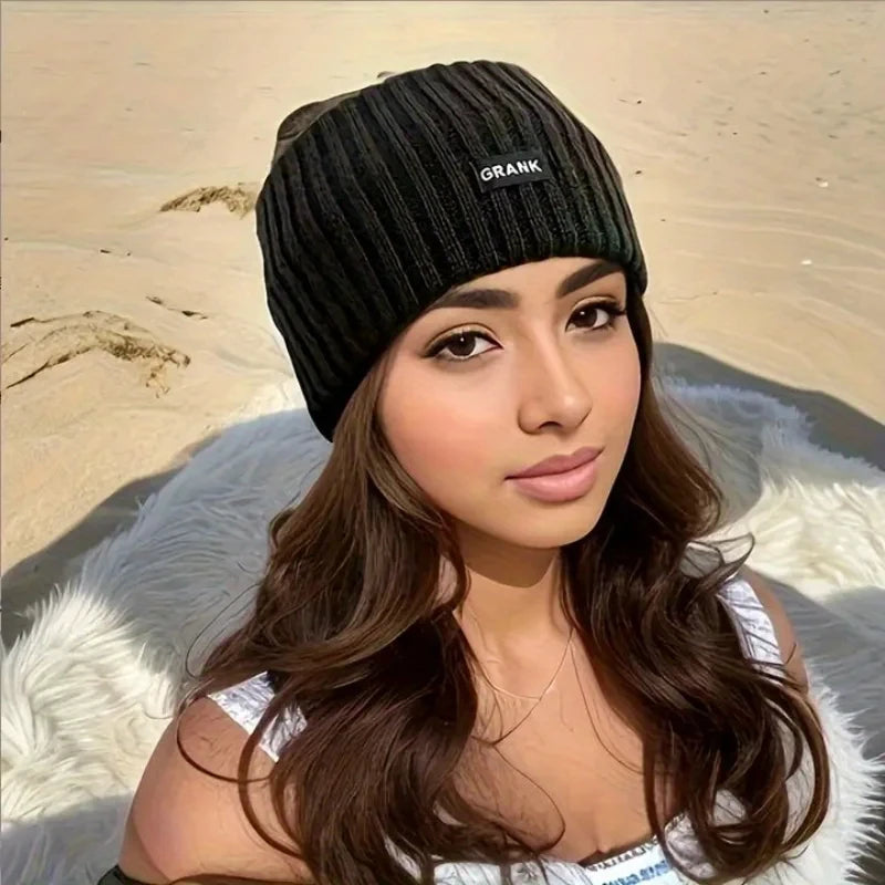 A woman wearing a black knitted winter headwrap and a white top, posing outdoors on sand.