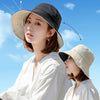 A woman wearing a wide brim bucket hat and white traditional clothing outdoors under a blue sky.