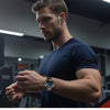 Ein Mann mit dunkelblauem Shirt und Smartwatch blickt zur Seite im Fitnessstudio.