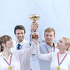 Four people holding a gold trophy and medals with ribbons in a bright indoor setting