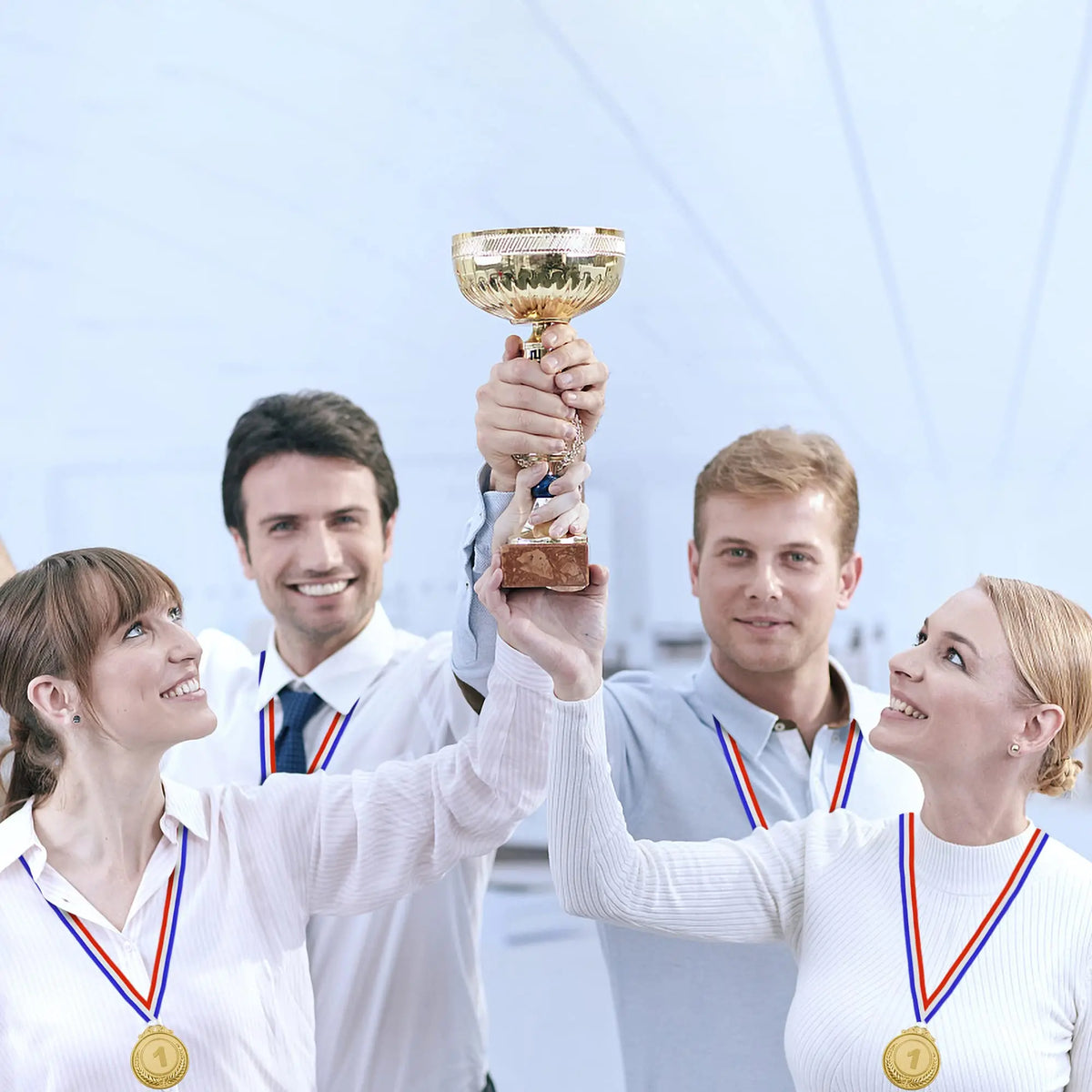 Four people holding a gold trophy and medals with ribbons in a bright indoor setting