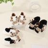 A pair of cartoon cow winter home slippers in white and black with brown accents.