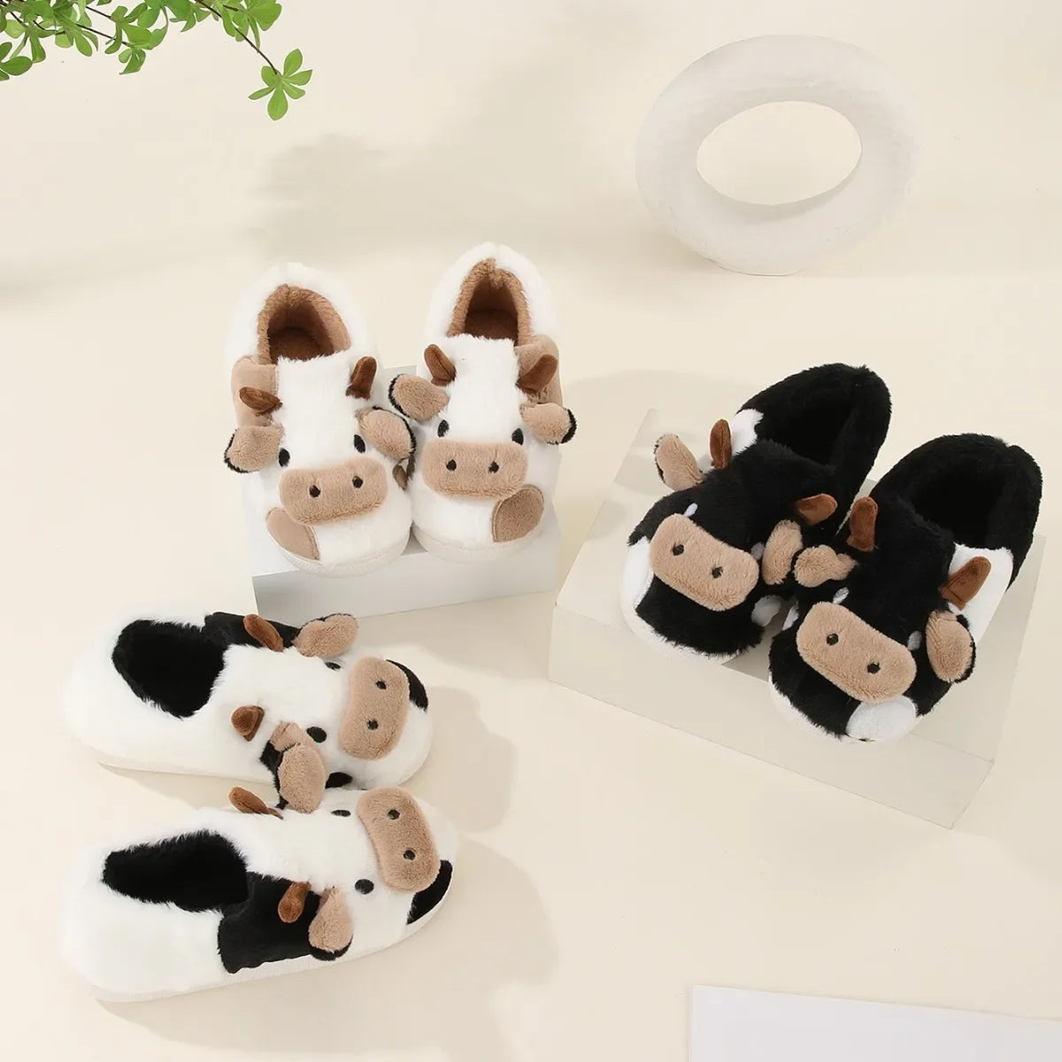 A pair of cartoon cow winter home slippers in white and black with brown accents.