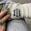 A hand wearing a white knitted sock with black embroidered text asking What's for snack today?