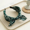 A dark green paisley bandana headband tied in a bow, displayed on a light tray.